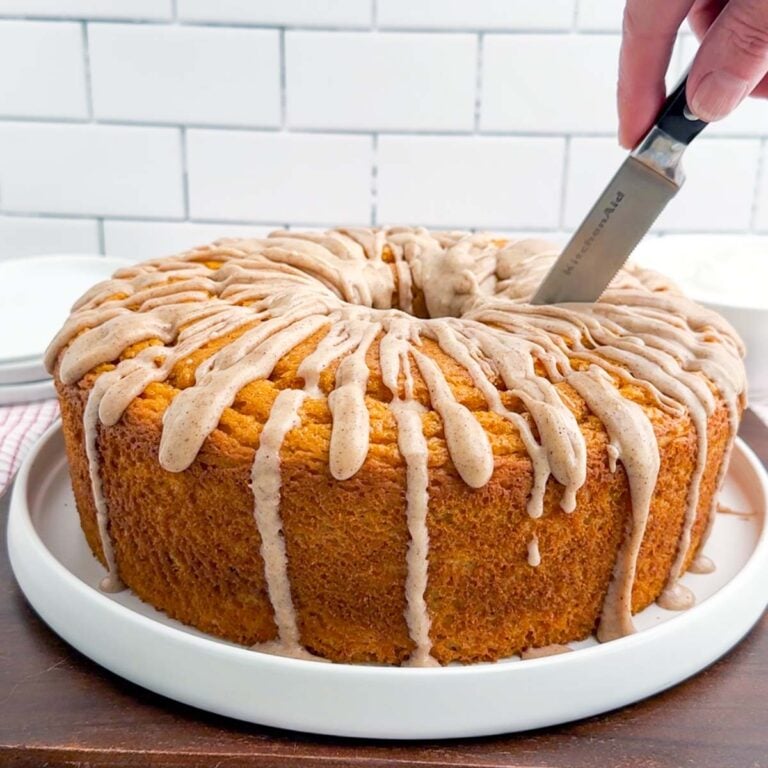 knife cutting into pumpkin angel food cake with cinnamon icing.