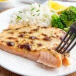 fork breaking off a bite of salmon with mayonnaise.