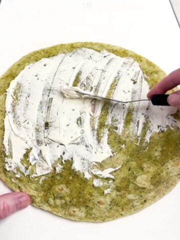 offset spatula spreading cream cheese on a large flour tortilla.
