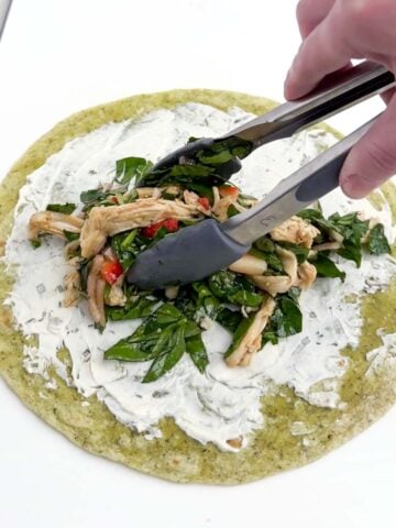tongs placing filling in the center of a large flour tortilla.