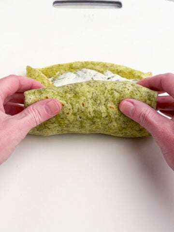 hands folding up the bottom of the tortilla over the filling.