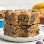 two banana blondies with the corner bites taken out stacked on a white plate.