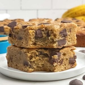 two banana blondies with the corner bites taken out stacked on a white plate.