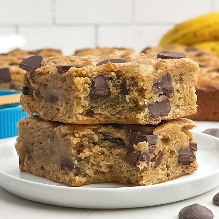 two banana blondies with the corner bites taken out stacked on a white plate.