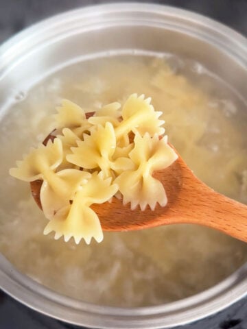 wooden spoon lifting pasta from a boiling pot of water.