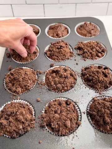 hand sprinkling streusel topping on top of muffin batter.