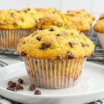 a chocolate chip cake mix muffin on a white plate with a wire rack of more chocolate chip muffins in the background.