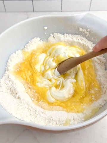 wooden spoon stirring lemon cake mix muffin batter in a white bowl.