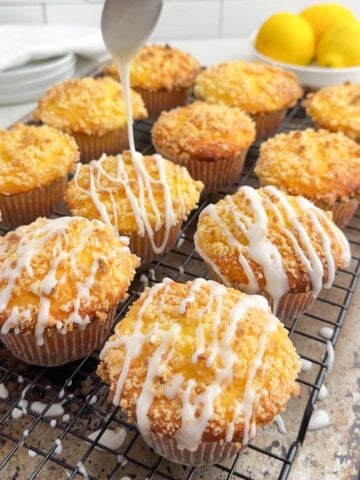 spoon drizzling lemon glaze on lemon cake mix muffins with streusel on a wire baking rack.