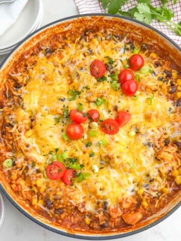 cheesy Mexican chicken and rice topped with tomatoes, green onions, and cilantro in a Dutch oven.