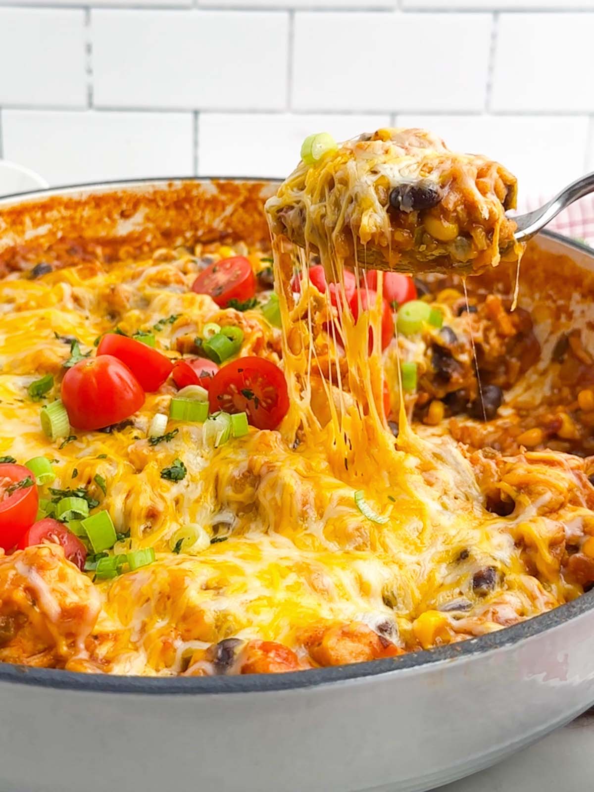 spoon lifting up a gooey, cheesy serving of Mexican chicken and rice from a Dutch oven.