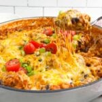 spoon lifting up a gooey, cheesy serving of Mexican chicken and rice from a Dutch oven.