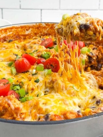 spoon lifting up a gooey, cheesy serving of Mexican chicken and rice from a Dutch oven.