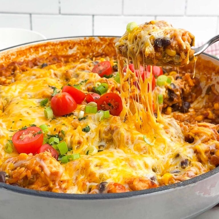 spoon lifting up a gooey, cheesy serving of Mexican chicken and rice from a Dutch oven.