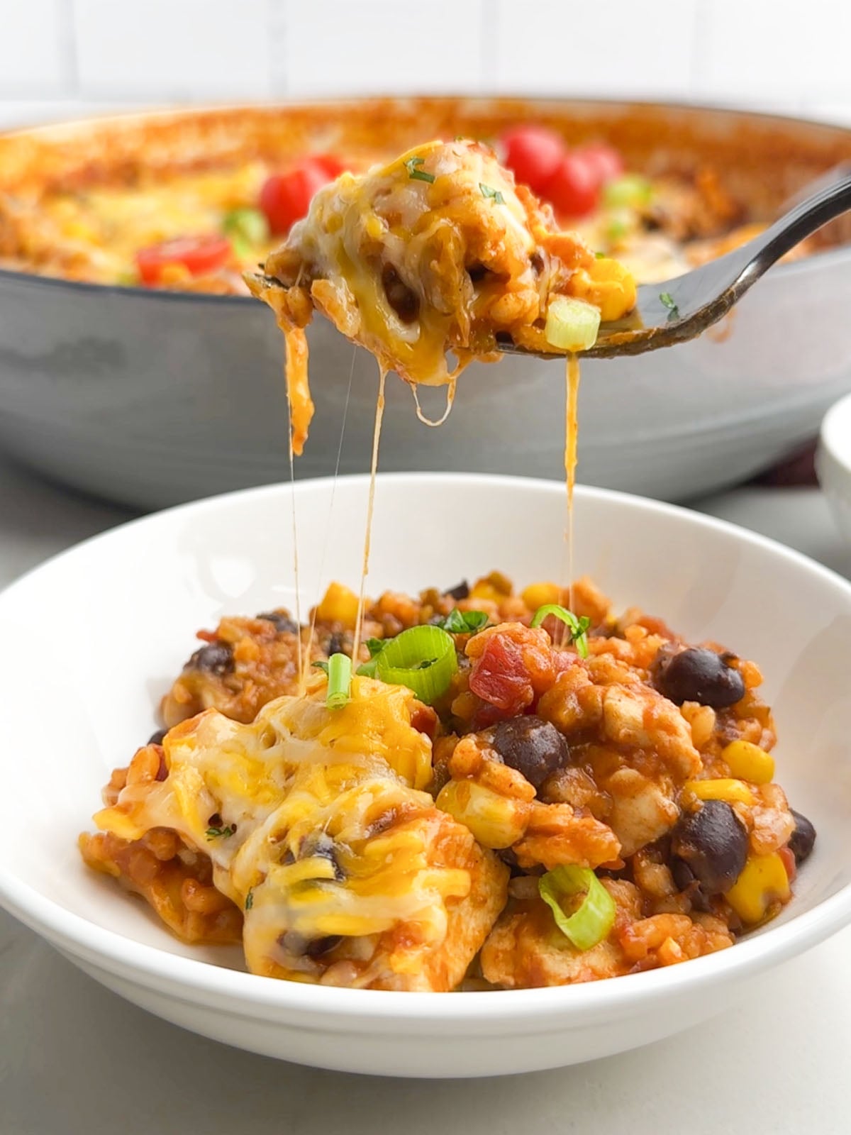 fork lifting up a gooey, cheesy bite of Mexican chicken and rice from a white bowl.