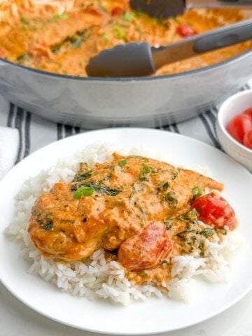 sundried tomato pesto chicken with spinach and tomatoes on a white plate.