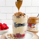 spoon drizzling melted almond butter over almond butter overnight oats with berries in a mason jar.