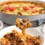 fork lifting a bite of cheesy ground beef salsa rice with beans and corn from a white bowl.