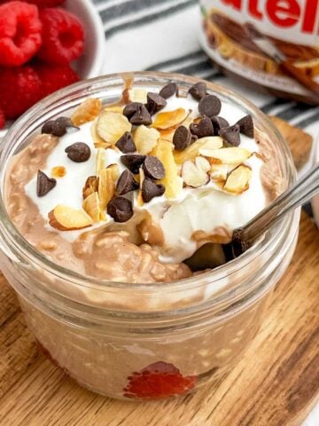Nutella overnight oats topped with chocolate chips and nuts in a mason jar.
