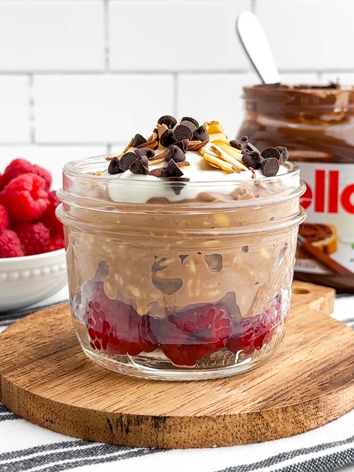 Nutella overnight oats topped with chocolate chips and nuts in a mason jar.