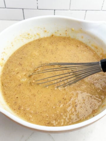 pineapple bread pudding custard mixture in a white bowl with a whisk.