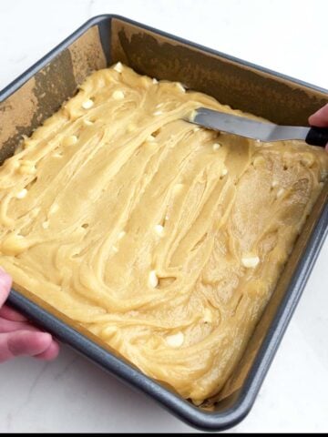 hand holding spatula smoothing white chocolate brownie batter in a baking pan.