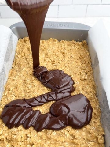 chocolate pouring over the oatmeal crust for chocolate revel bars.