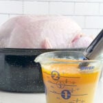 turkey injection liquid and an injector in a measuring cup in front of a turkey in a roaster pan.