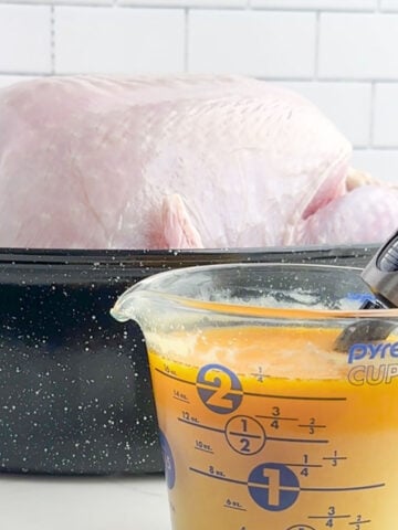 turkey injection liquid and an injector in a measuring cup in front of a turkey in a roaster pan.