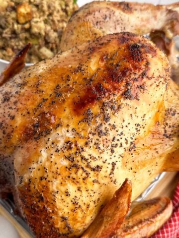 a whole roasted turkey with a bowl of stuffing in the background.