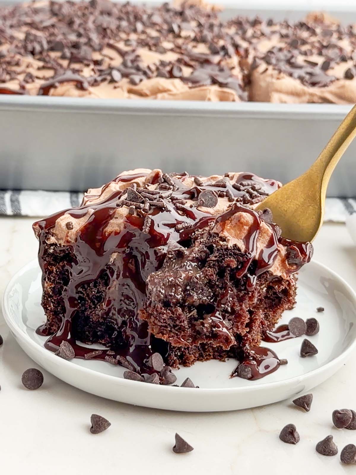 piece of chocolate poke cake on a white plate.