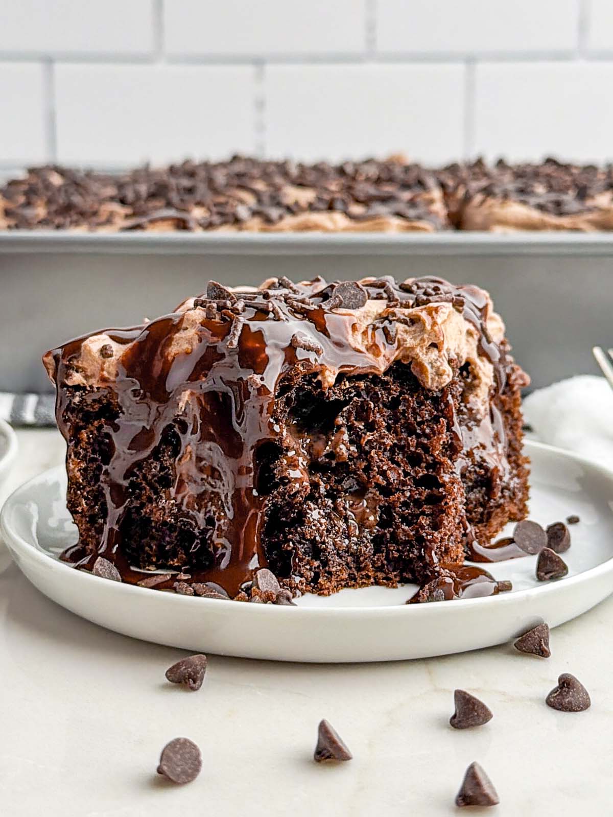 piece of chocolate poke cake on a white plate.