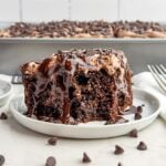 piece of chocolate poke cake on a white plate.