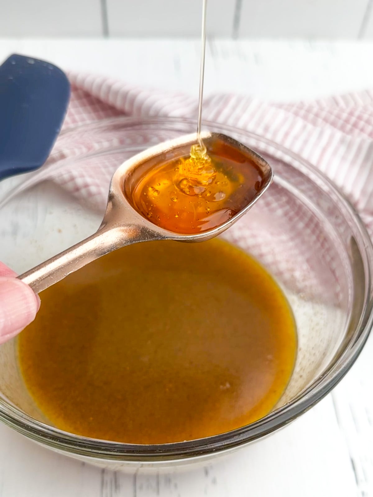 honey drizzling into a tablespoon over a bowl of vinaigrette.