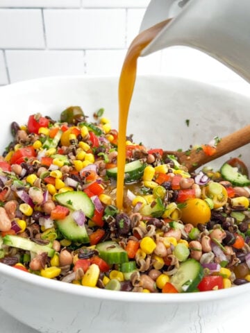 pouring dressing over corn and wild rice salad in a white bowl.