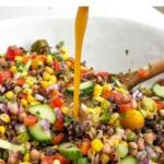 pouring dressing over corn and wild rice salad in a white bowl.